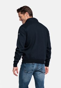 Marine pullover trui met hoge kraag, geribbelde manchetten en zoom; gestructureerde stof met een gladde afwerking, gedragen met lichtblauwe jeans.