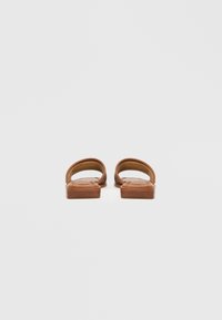 Brune l�ædersandaler med åben hæl og flettet remdesign. Flad sål med tekstureret finish. Minimalistisk stil, neutral farve.