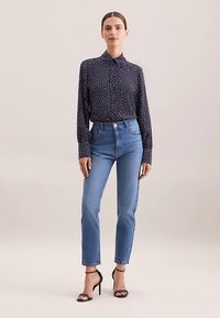 Blusa blu navy con pois bianchi, maniche lunghe e colletto, abbinata a jeans azzurri a vita alta e sandali neri con cinturini.