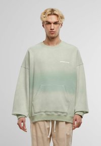 Hanorac supradimensionat verde dintr-un amestec de bumbac, cu un gradient de culori, buzunar frontal și logo-ul "ANOTHER COTTON" în alb.