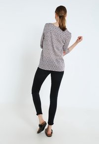 Blouse à manches longues crème avec un motif géométrique, associée à un jean skinny noir et des sandales foncées, mettant en valeur une coupe décontractée et un tissu doux.