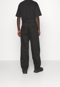 Svarta bomullsbukser med avslappnad passform, med rak bendesign, två bakfickor och en midja med bälteslås, sedd bakifrån.