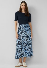 Marineblauw T-shirt met korte mouwen gecombineerd met een lichte, enkel-lange rok met een blauw bloemenpatroon op een lichtblauwe achtergrond. Witte sneakers.