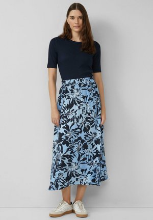 Marineblauw T-shirt met korte mouwen gecombineerd met een lichte, enkel-lange rok met een blauw bloemenpatroon op een lichtblauwe achtergrond. Witte sneakers.