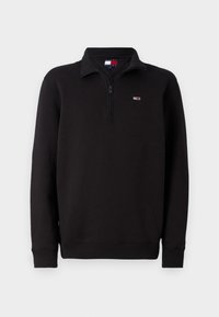 Sudadera negra con cuello de cremallera de un cuarto, puños y dobladillo acanalados. Presenta un pequeño logo en el lado izquierdo del pecho. Está hecha de una tela texturizada.
