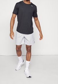 Czarna koszulka z krótkim rękawem z logo, jasnoszare szorty, białe skarpetki i buty sportowe. Skupienie na projektowaniu i dopasowaniu odzieży sportowej.