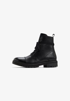 Bottines en cuir noir avec une texture lisse, bout rond et lacets sur le devant. Présente des œillets en métal et une semelle en caoutchouc renforcé.