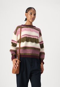 Strikkegenser med horisontale striper i rosa, krem og olivengrønn med teksturerte mønstre, kombinert med en liten brun crossover-veske.