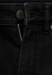 Läskut, svart denimjeans i närbild, med en metallknapp och dragkedja, synlig sömnad och en jämn textur.