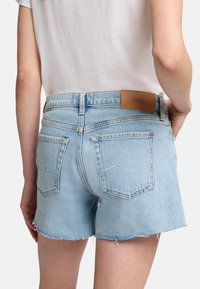 Ljusblå denimshorts med fransade kanter, med två bakfickor och en bälteetikett i ljusläder.