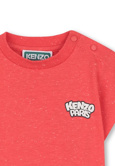 T-shirt en tissu rouge à pois avec un col rond, comportant des boutons-pression sur l'épaule et un logo "KENZO PARIS".
