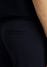 Pantalones azul marino texturizados con un bolsillo trasero con una costura horizontal, diseño ajustado con trabillas y una cinturilla suave.