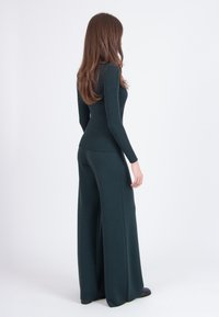 Green ribbed knit top paired with loose, wide-leg pants, showcasing a fitted silhouette at the waist and soft texture.