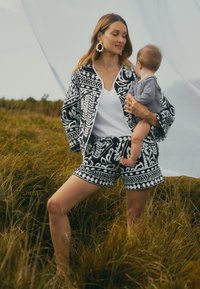 Schwarzes und weißes gemustertes Jacken- und Shorts-Set aus leichtem Stoff. Die Jacke hat einen rundem Kragen und einen lockeren Schnitt.