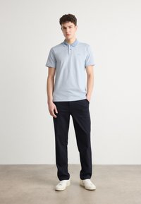 Lyseblå polo med krage og hvite detaljer, kombinert med mørke bukser og hvite joggesko. Glatt stoff og tettsittende design.