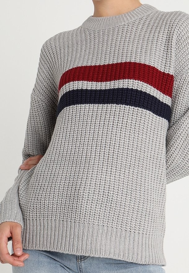 Szary dzianinowy sweter o prążkowanej fakturze, z czerwono-biało-granatowymi poziomymi paskami na wysokości klatki piersiowej. Okrągły dekolt i luźny krój.