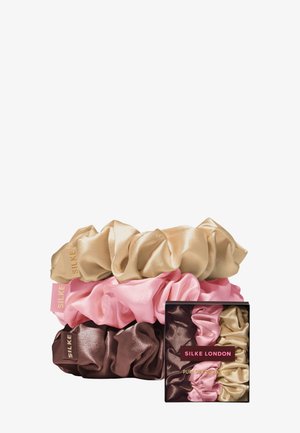 Trois chouchous en soie beige, rose et marron empilés à côté d'une boîte assortie étiquetée Silke London Pure Silk Scrunchies.