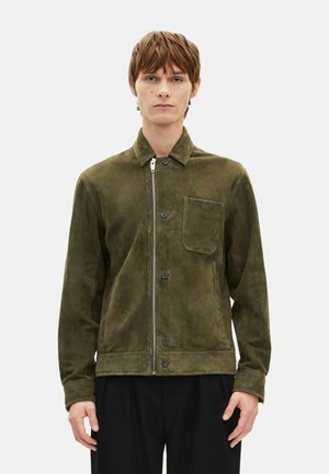 Zamszowa kurtka oliwkowozielona z przednim suwakiem, zatrzaskami i kieszenią na piersi. Posiada spiczasty kołnierz i długie rękawy.