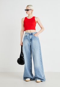 Röd kortbukad linne, vida ljusblå denimjeans, vita sneakers och en liten svart handväska. Slätt tyg, avslappnad passform och ljus tvätt.