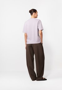 Lawendowa bluzka z krótkimi rękawami zestawiona z luźnymi, brązowymi spodniami o teksturze. Stylizacja charakteryzuje się swobodnym krojem i prostym wzornictwem bez ozdób.