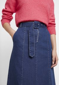Mörkblå denim-midi kjol med bälte i midjan och dragkedjedetalj. Matchad med en mjuk rosa tröja. Har sido fickor och sömnadsdetaljer.