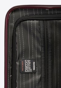 Black interior of a suitcase featuring smooth fabric with vertical stripes and mesh pocket. Includes a branded label with care instructions.