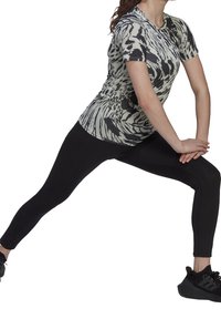 Person der bærer sorte leggings og en mønstret kortærmet skjorte, strækker benene i en sidelunge med hænderne samlet foran.