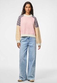Roze gemêleerd trui met gebreide mouwen in navy en oranje, gecombineerd met lichtblauwe wijde jeans en beige schoeisel.