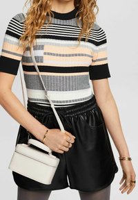 Monivärinen ribbitty neulepaita lyhyillä hihoilla, jossa on mustia, harmaita, persikkavärisiä ja valkoisia raitoja. Yhdistetty mustien tekonahkashortsien ja valkoisen laukun kanssa.