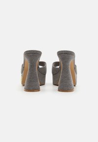 Des chaussures à talons hauts en tissu gris présentent un talon courbé et un design à dos ouvert. La texture est lisse avec peu d'embellissements et une semelle couleur beige.