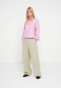 Rozā garām piedurknēm krekls ar pogām, apkakli un brīvu piegriezumu, kombinēts ar zaļām, plašām pleda biksēm ar augstu vidukli. Melni apavi.