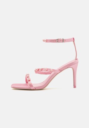 Różowe sandały na wysokim obcasie z wieloma paskami ozdobionymi okrągłymi perłowymi akcentami. Gładka satynowa tekstura, spiczasty czubek, regulowany pasek w kostce.