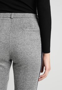 Šedé herringbone kalhoty s hladkým povrchem, obsahující zadní kapsu a námořnické boční pruhy, kombinované s černým žebrovaným topem.