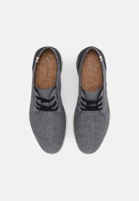 Pár šedých textilních ležérních šněrovacích bot s černými tkaničkami a korkovými stélkami na bílém pozadí.