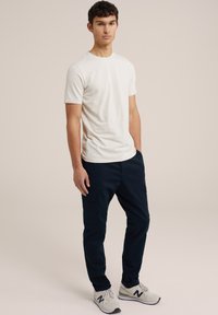 Tricou alb cu mânecă scurtă, asortat cu pantaloni cargo negri închis. Modelul poartă adidași gri deschis cu accente întunecate. Design simplu și funcțional.