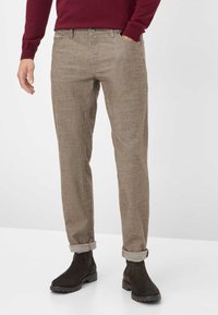 Braune, strukturierte Hose mit geradem Schnitt, umgeschlagenen Säumen und Fronttaschen, kombiniert mit dunkelbraunen Stiefeletten.