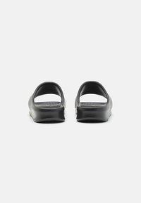 Sandale negre cu talpă plată, având un design minimalist, spate deschis, textură netedă și o branduire subtilă pe tălpile interioare.