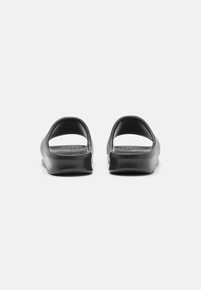 Sandales noires à glissière avec un design minimaliste, un dos ouvert, une texture lisse et un branding discret sur le semelage.