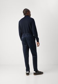 Polo en maille bleu marine et pantalon en velours côtelé bleu marine assorti, vus de l'arrière, avec des baskets noires présentant des accents blancs et marron.