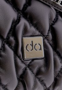 Bolso de cuero negro acolchado con una etiqueta de metal brillante. La textura presenta costuras prominentes y un diseño acolchado.