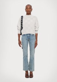Maglione grigio chiaro con texture e motivo a scacchi, abbinato a jeans svasati di lavaggio medio e sandali neri con cinturini. Borsa nera con hardware.