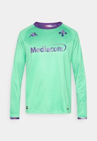 Nogometni dres z dolgimi rokavi iz mint zelene mrežaste tkanine s vijoličnimi poudarki in logotipom. Ima okrogel izrez in teksturiran vzorec povsod.