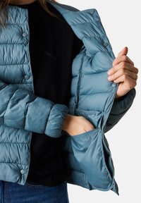 Helle blaue Steppjacke mit einem strukturierten, gesteppten Design. Verfügt über Druckknöpfe und Innentaschen zur Aufbewahrung. Weiches, glattes Material.