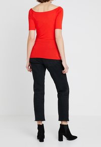 Haut rouge ajusté à manches courtes avec un col large, associé à un jean noir raccourci et des bottines noires. Le tissu semble lisse.