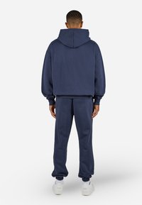 Marinebl�å hættetrøje og matchende joggers lavet af blødt stof, med elastiske mansjetter og talje, set bagfra.