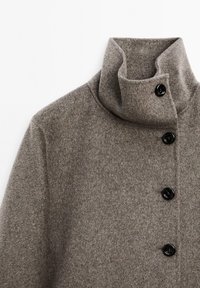 Cappotto di lana grigio con colletto alto, cinque bottoni neri e finitura morbida e testurizzata. Punto focale su un design minimalista e una silhouette moderna.