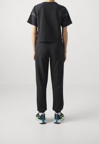 Zwart cropped T-shirt met korte mouwen, gecombineerd met zwarte joggers. De outfit heeft een gladde textuur en een minimalistisch ontwerp, gedragen met sportieve schoenen.