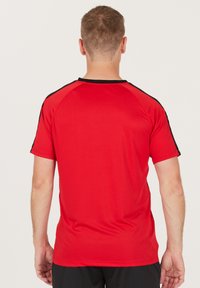 Punainen urheilupaita, jossa on pyöreä musta kaulus ja mustat yksityiskohdat harteilla; valmistettu sileästä, kevyestä kankaasta.