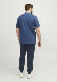 Mörkblå pikétröja med vita detaljer, kombinerad med mörkblå joggers. Tyget verkar mjukt, med en avslappnad passform och en enkel design.