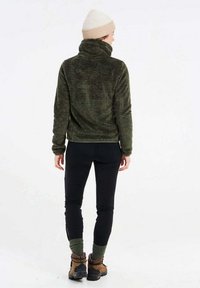 Olijfgroene fleecjas met hoge kraag, zwarte leggings en bruine wandelschoenen; toont een zachte textuur en een getailleerd ontwerp.
